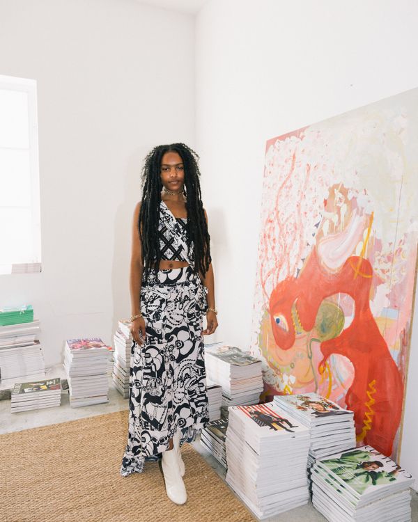 Destiny Joseph posed next to piles of magazines and art canvases 