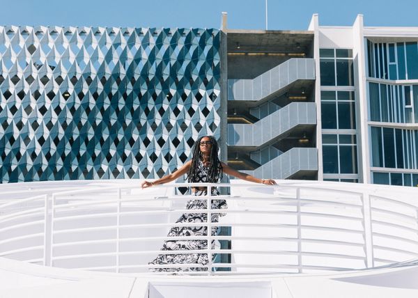 Woman posed on a white bridge with a geometric building behind her