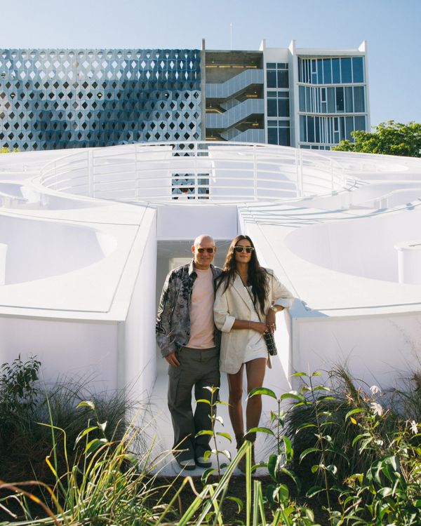 A couple posed next to a white circular structure in front of a geometric building