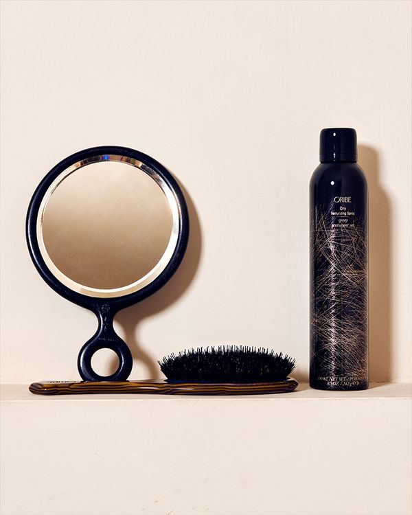 Oribe texturing spray set next to a hand-held mirror and hair brush 