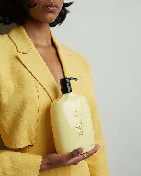 Girl wearing a yellow blazer holding the Oribe Alchemy Shampoo bottle