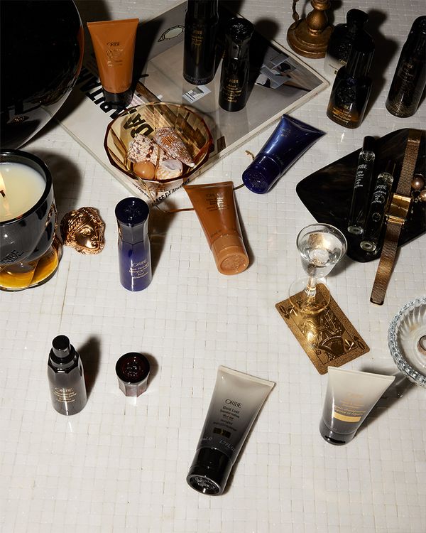 A variety of Oribe products on a surface next to fashion accessories and decor pieces 