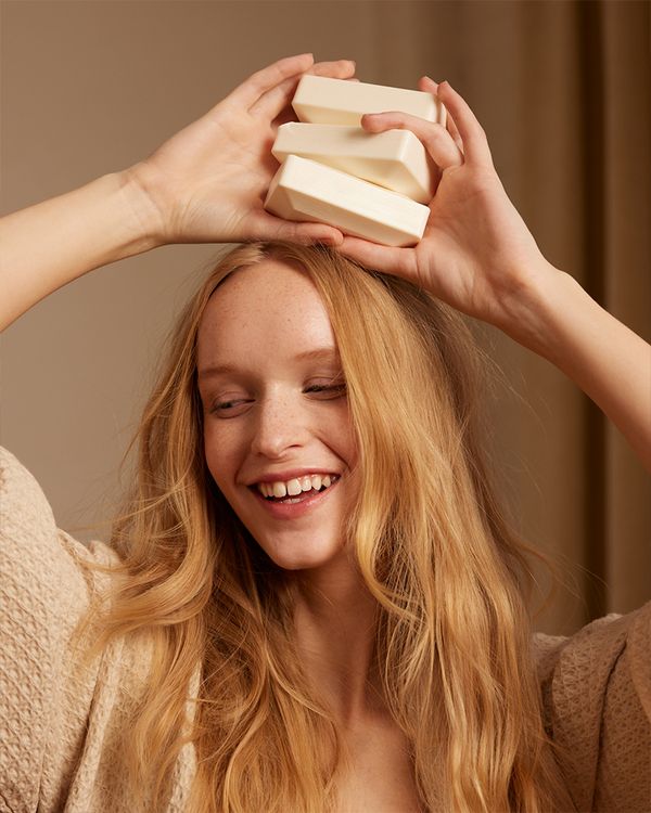 Girl with long blonde hair posed smiling and holding three Oribe soap bars above her head